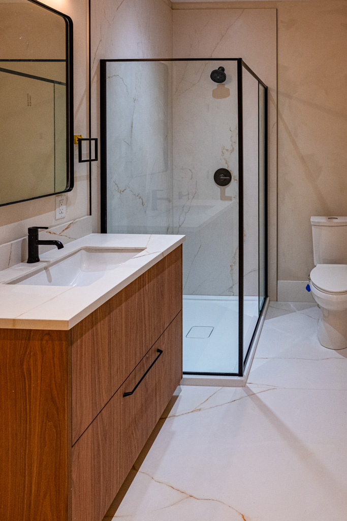 Modern bathroom with wood vanity, glass shower, and marble tile